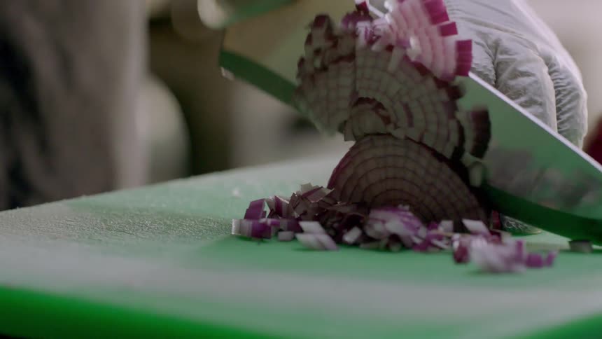 A chef is cutting red onion on a cutting board