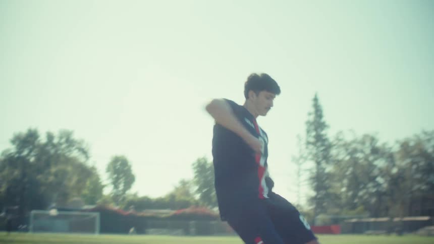 A determined soccer player in a USA uniform powerfully kicks a ball on a sunny field in slow motion
