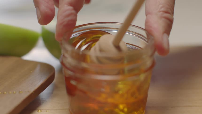 A person stirs honey in a jar with a honey dipper