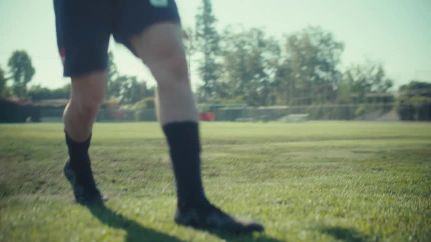 Low angle slow motion shot of a soccer player's feet running up and kicking a ball on a sunny green field