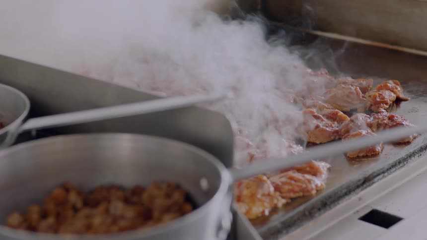 Food is cooking and steaming on a griddle during the day