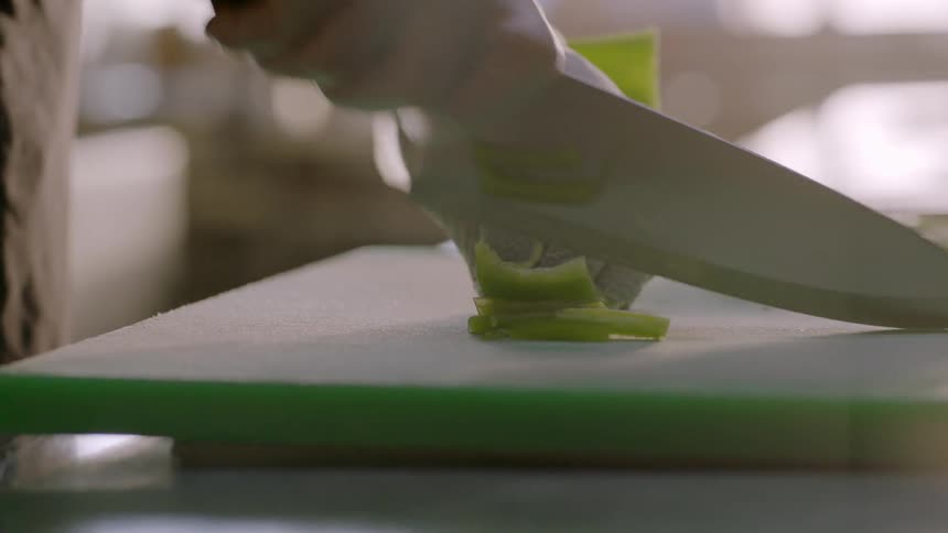 A restaurant worker dices peppers on a cutting board