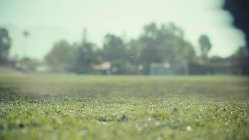 A soccer player's feet run up and powerfully kick a soccer ball in slow motion on a grassy field