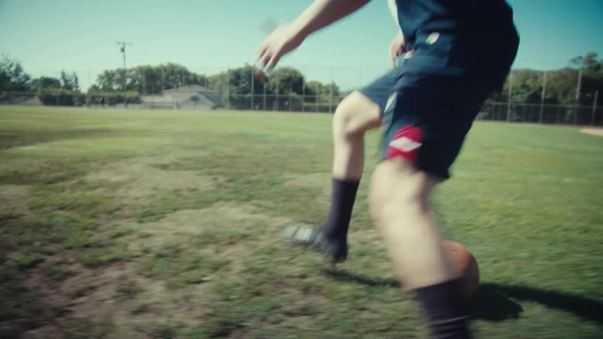 Close-up slow-motion shot of a male soccer player dribbling a vintage-style ball on a sunny day