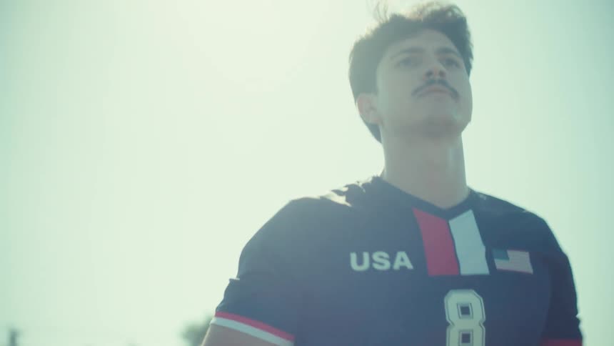 A determined young soccer player in a USA jersey walks across a sunny field in a cinematic slow motion shot