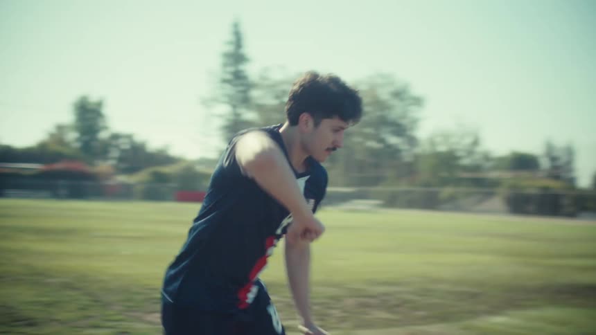 A determined young soccer player in a USA jersey begins to run across a sunny field in slow motion