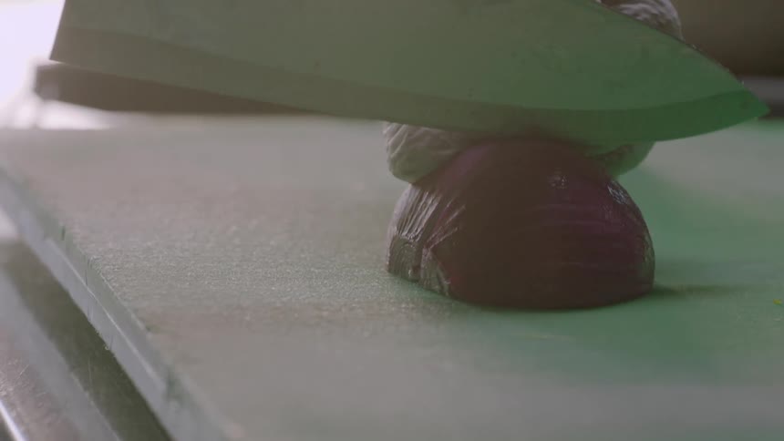 A restaurant worker dices an onion on a cutting board