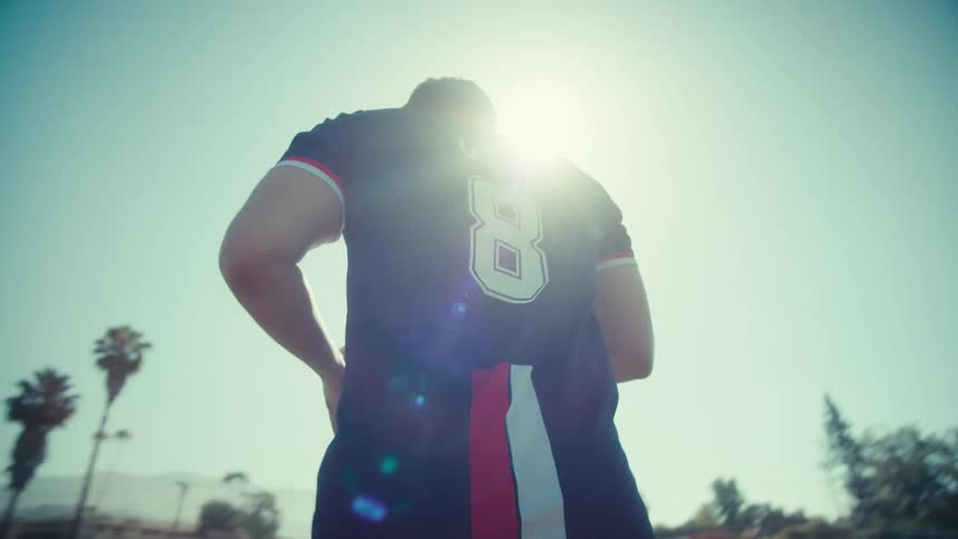 A young soccer player in a USA jersey walks across a grassy field in slow motion on a sunny day