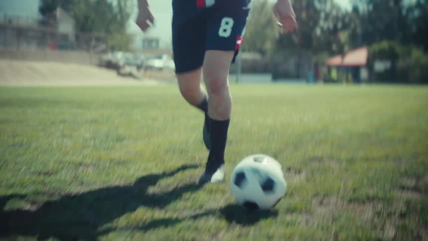 Skilled soccer player showcases impressive footwork while dribbling a ball down a sunny field in slow motion