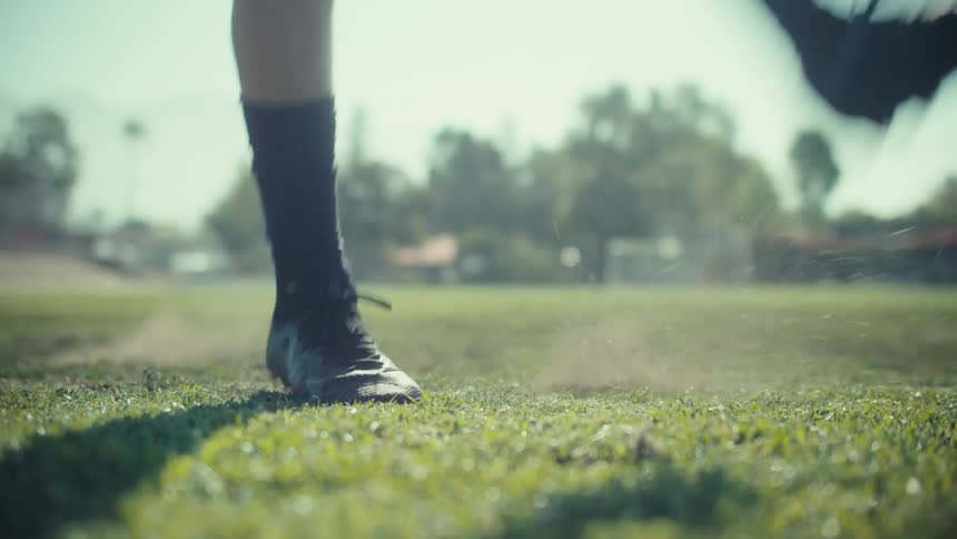 Slow motion close-up of a soccer player's cleat kicking a soccer ball on a grassy field on a sunny day