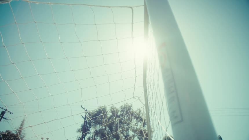 Low angle slow motion shot of a soccer ball hitting the back of the net for a goal on a sunny day