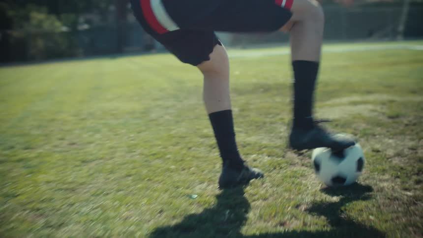 Slow-motion close-up of a soccer player's feet dribbling a ball down a grassy field before kicking it into the goal