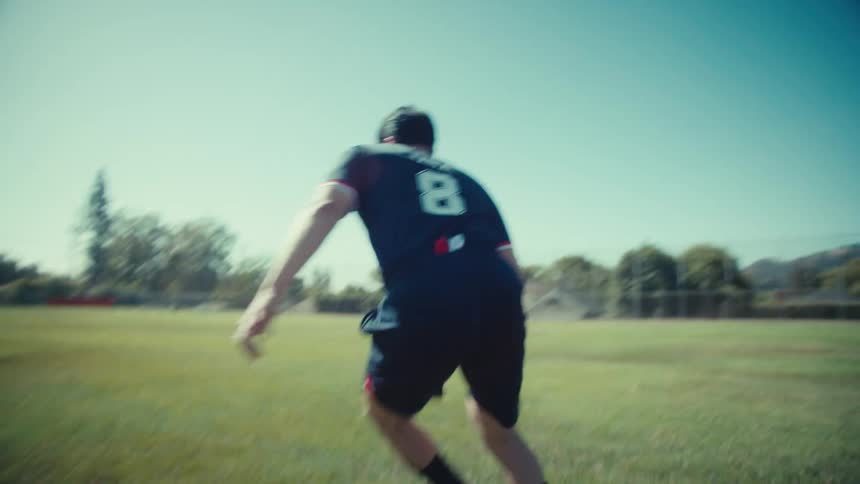 A soccer player in a USA jersey dribbles a vintage ball across a sunlit field in a dynamic slow-motion follow shot