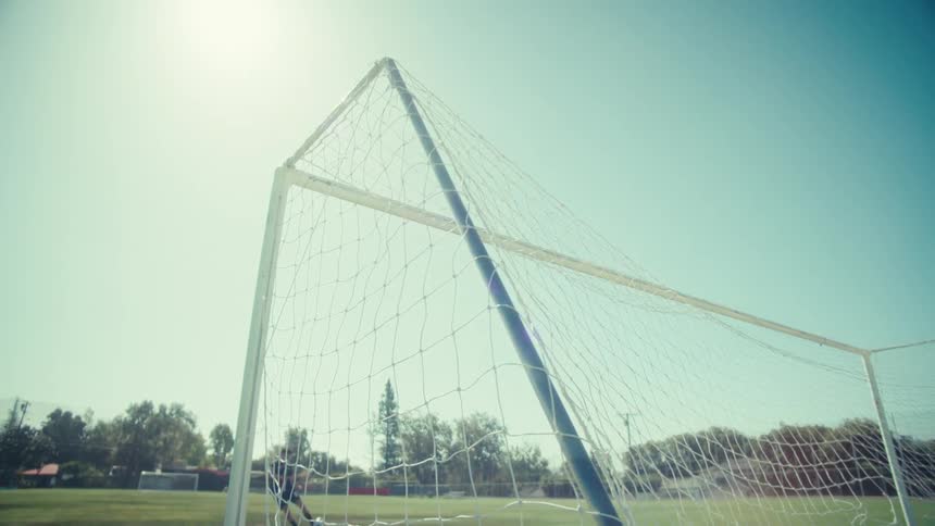 Slow motion close-up of a soccer ball hitting the back of the net on a sunny day