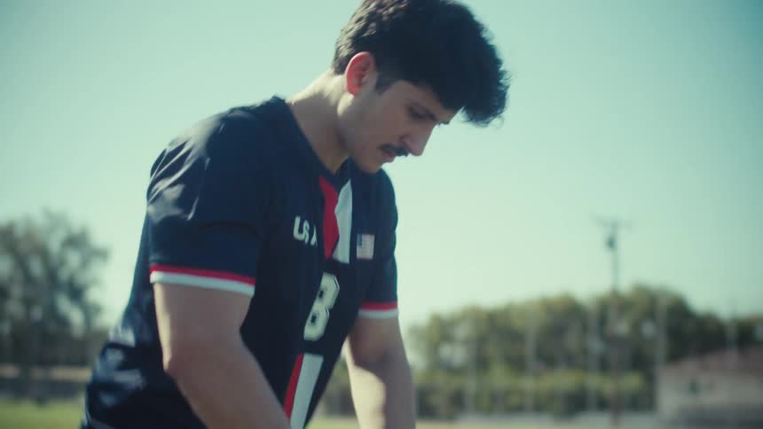 A focused soccer player in a USA jersey walks onto a sunny field and places the ball down for a kick in slow motion