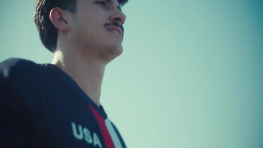 A determined USA soccer player walks across a sunlit field with a ball in slow motion