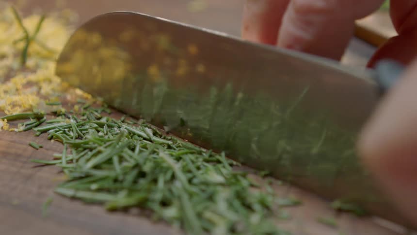 A person chops herbs with a large knife