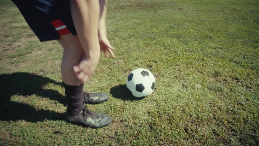 A soccer player in slow motion carefully places the ball on a sunny, green field, preparing for a kick
