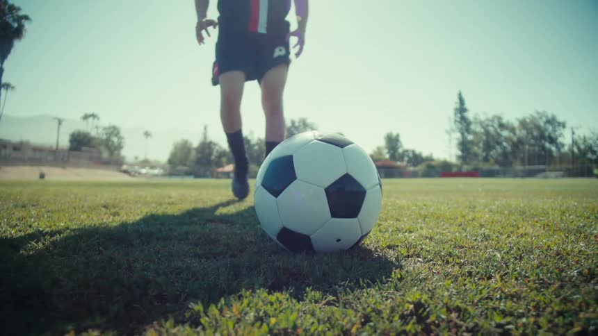 Low-angle slow motion shot of a soccer player placing the ball down and taking a powerful kick on a sunny field