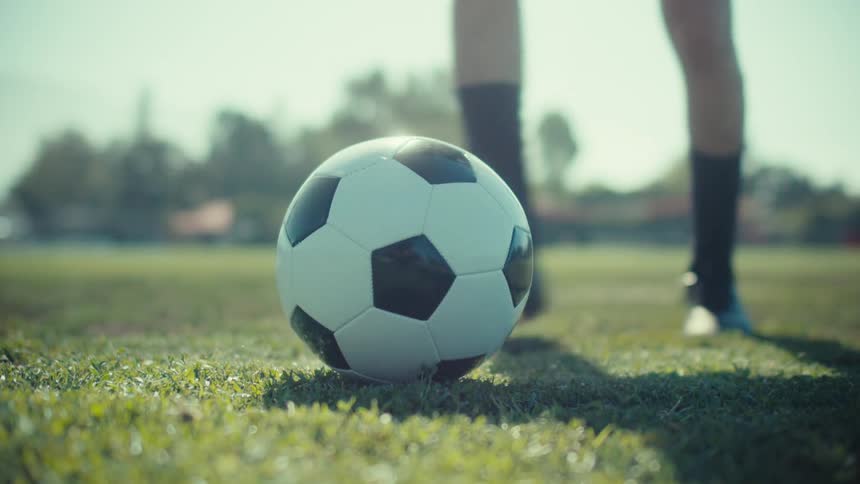 A soccer player in slow motion places a ball on the grass and kicks it on a sunny day