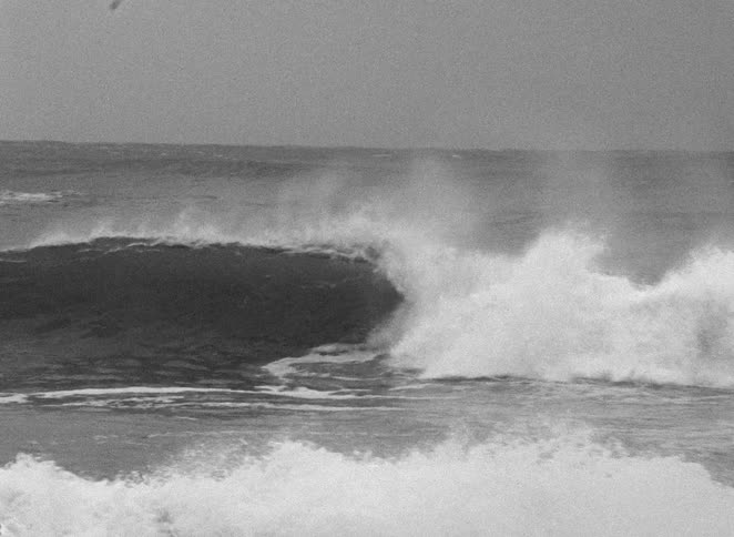 A surfer rides a powerful ocean wave before getting wiped out in this vintage black and white clip