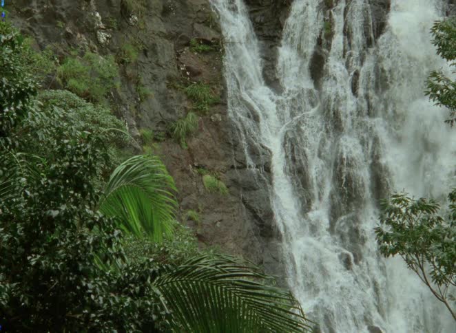 A powerful waterfall cascades down a rocky cliff face framed by lush green jungle foliage