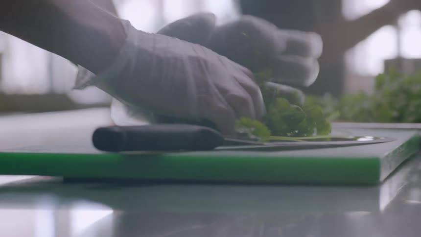 Person rolling up bundle of cilantro on cutting board in kitchen