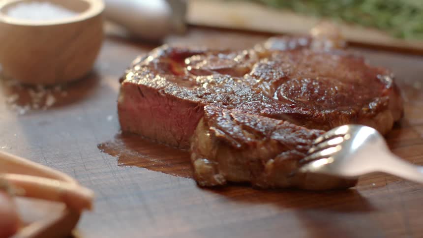A person forks a piece of steak from the platter