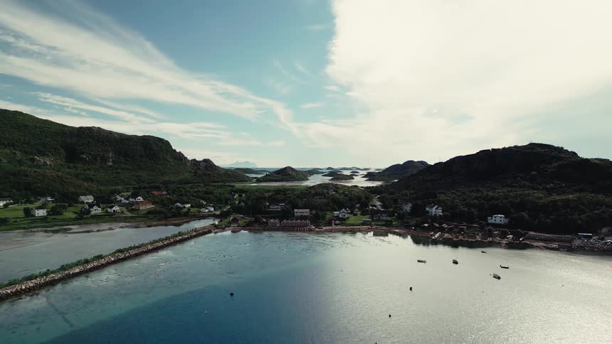 A serene aerial wide shot captures a picturesque coastal village nestled between lush green hills and a calm blue bay