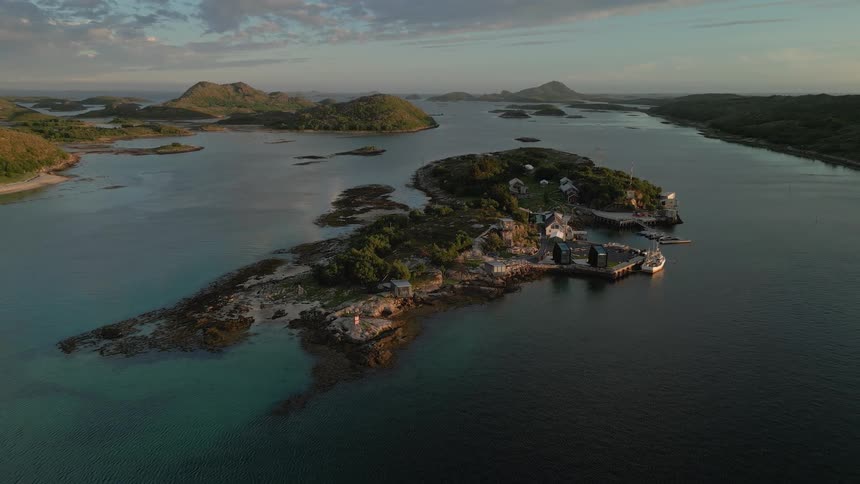 Static aerial view of a small, isolated island village nestled in an archipelago during a calm, golden sunset