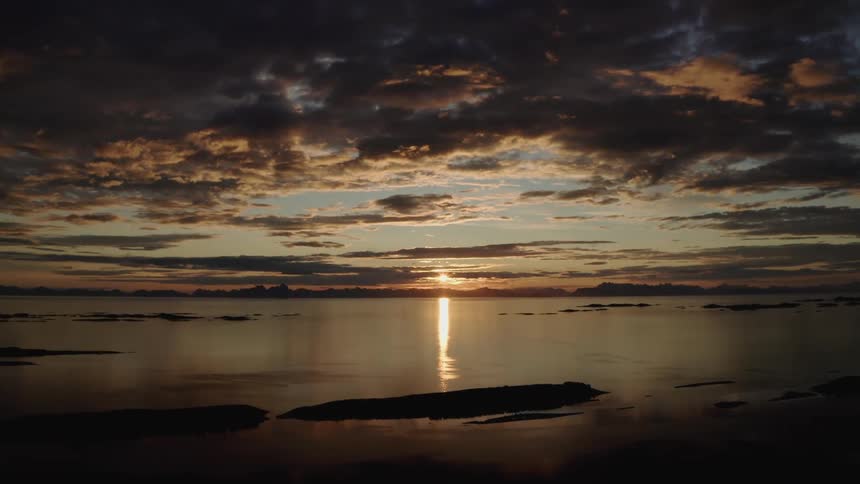 A stunning wide shot of a serene sunset over the ocean, with the sun's reflection shimmering on the water under a dramatic sky