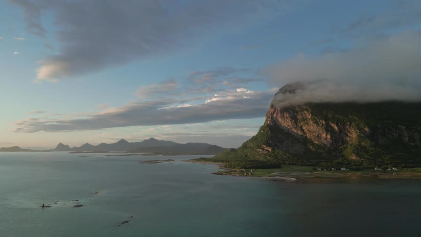 An awe-inspiring, static aerial view of a magnificent mountain in Lofoten, Norway, its peak enveloped by clouds during a serene sunset