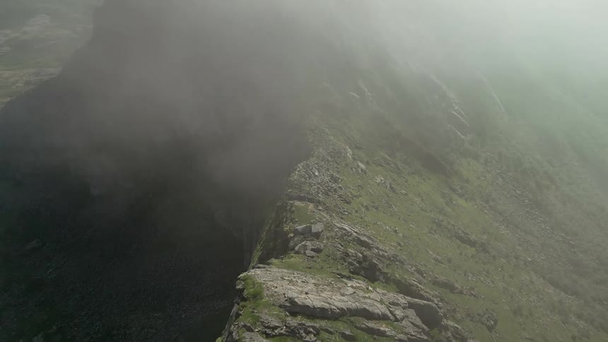 Awe-inspiring aerial view flying along a steep, rocky mountain ridge as the fog slowly clears