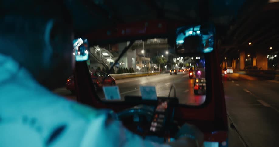 A point-of-view shot from inside a moving tuk-tuk as it drives through the bustling city streets of Bangkok at night