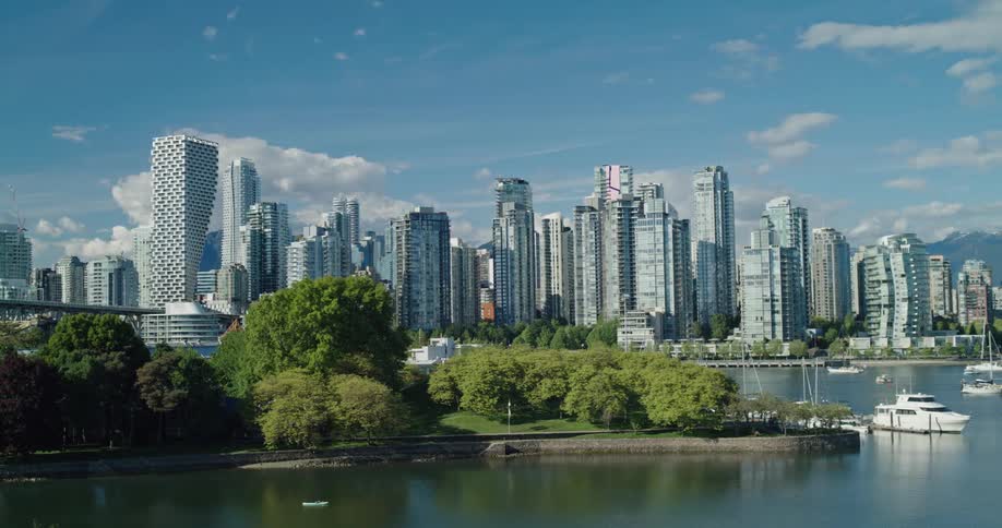 A slow pan across the beautiful Vancouver, Canada skyline with lush green parks and boats in the harbor on a bright, sunny day
