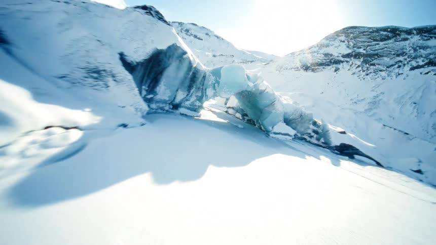 An exhilarating FPV drone flight soars over a vast glacier before diving through a beautiful blue ice cave on a sunny day