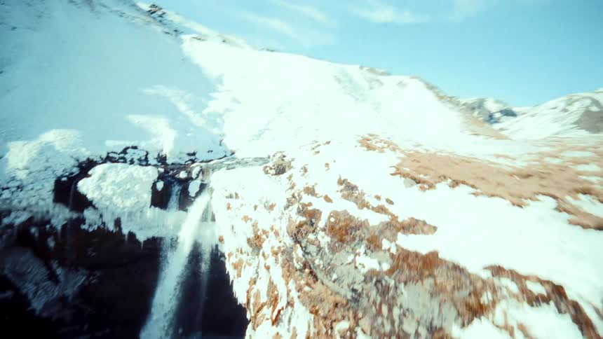 A thrilling first-person view drone dive reveals a hidden waterfall in a vast, snow-covered canyon on a sunny winter day