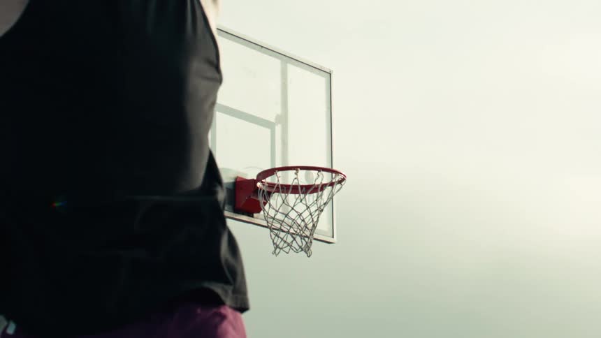 A basketball player with curly hair successfully makes a shot into the hoop in a dramatic slow-motion sequence