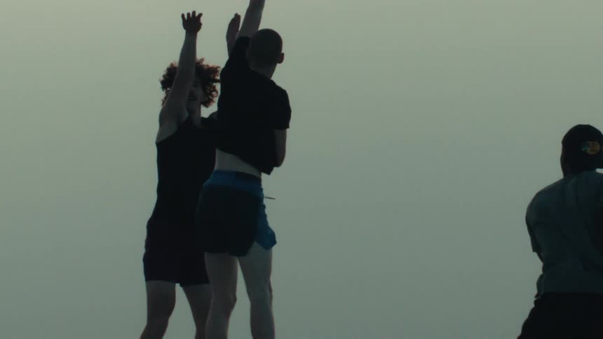 Silhouetted basketball players compete on an outdoor court as one jumps to shoot the ball in dramatic slow motion