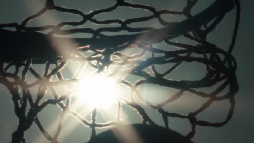 Dramatic slow-motion shot of a basketball scoring, backlit by a brilliant sun flare
