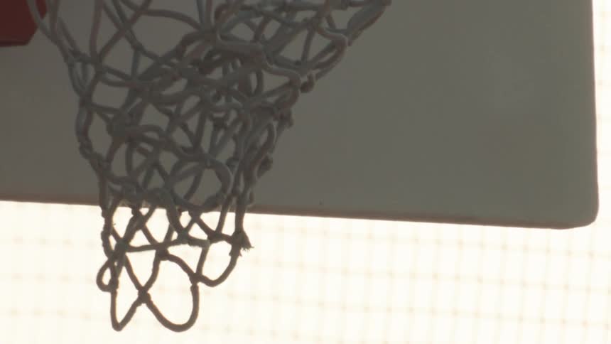 A silhouetted basketball swishes through the net in dramatic slow motion