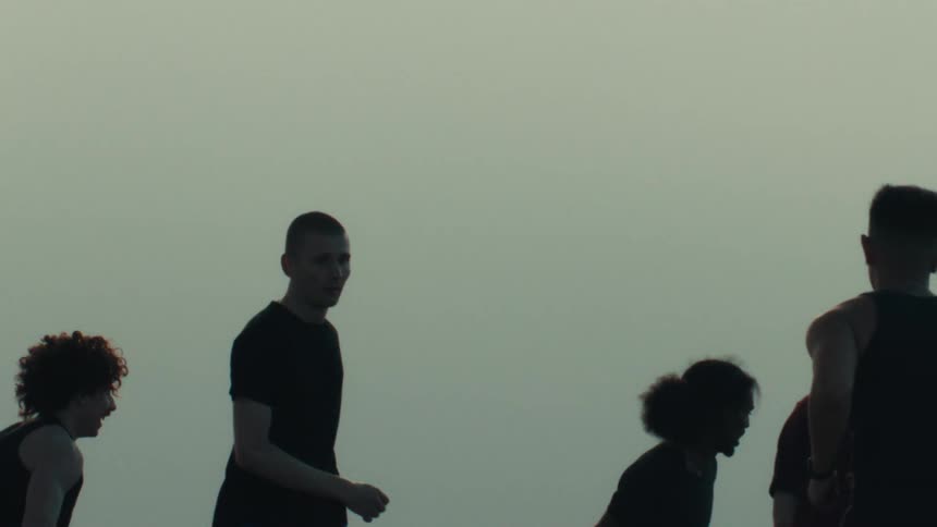 Silhouettes of a diverse group of young men playing basketball together in slow motion on an outdoor court at dusk