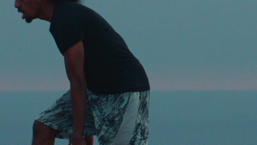 Close-up slow-motion shot of an athlete dribbling a basketball against a serene ocean background at dusk