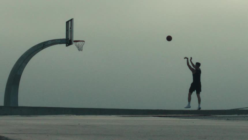Silhouette of a man shooting a basketball in super slow motion on an outdoor court