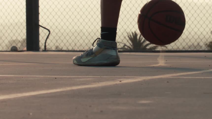 Slow motion close-up of a basketball player's sneakers while dribbling on an outdoor court at sunset