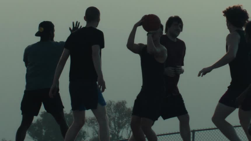 Silhouetted basketball players compete in a pickup game as one player jumps to take a shot in dramatic slow motion