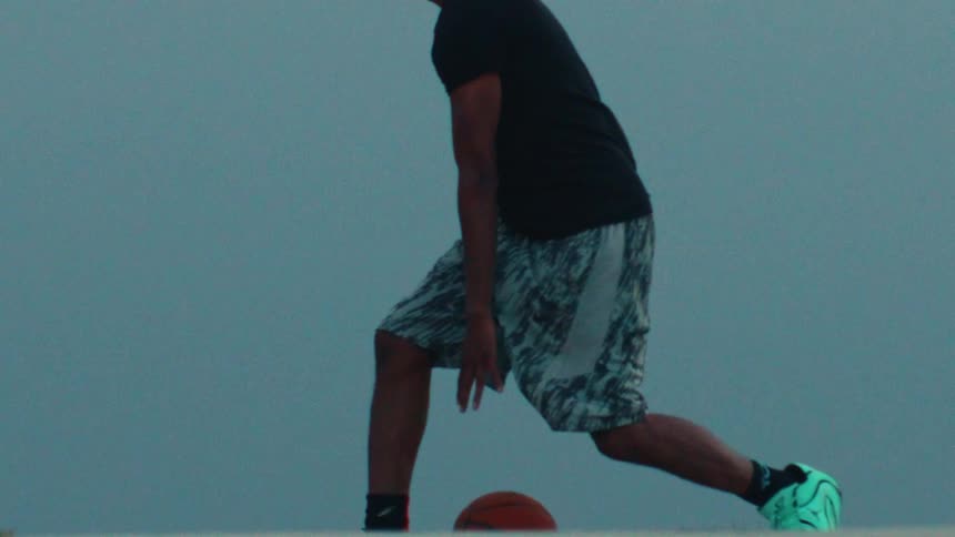 An athletic man practices his basketball dribbling skills in a dramatic slow-motion close-up