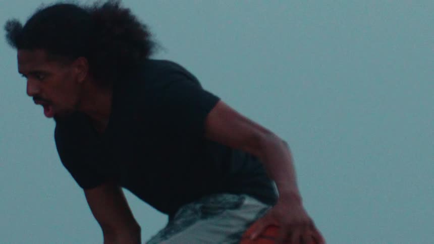 An athlete with long hair intensely dribbles a basketball in a dramatic slow motion shot