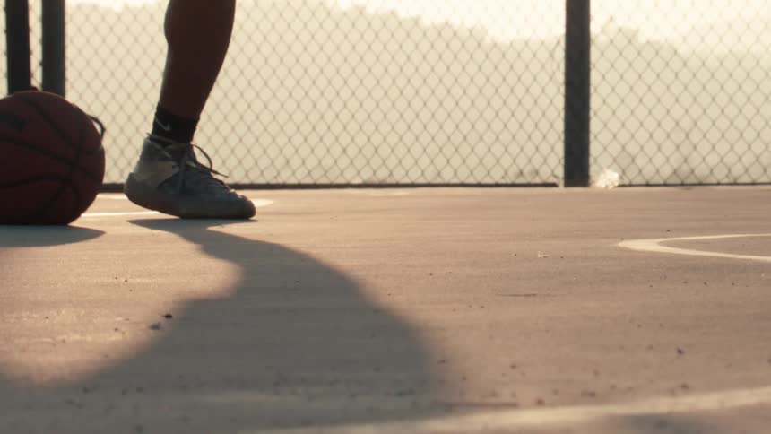 A basketball player's shoes are seen in extreme slow motion as they dribble a basketball on an outdoor court at sunrise
