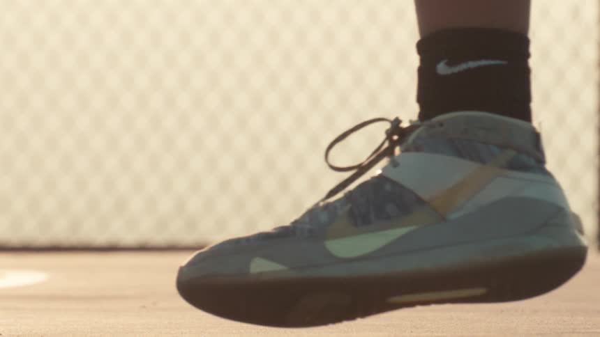 A close-up slow-motion shot of a basketball player's Nike shoe while they dribble the ball on an outdoor court